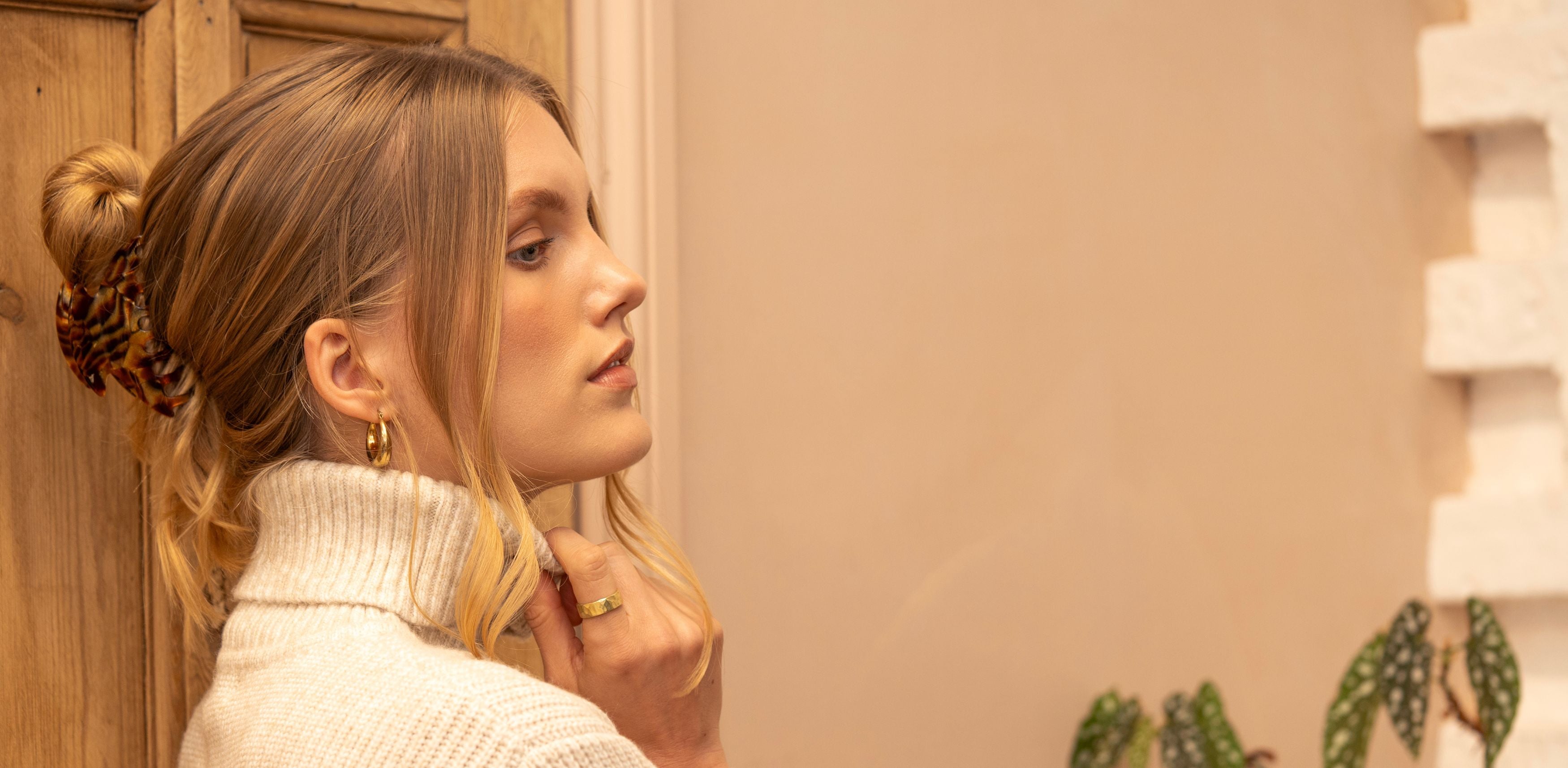 Woman in a white sweater standing in a room with wooden door and decorative elements.
