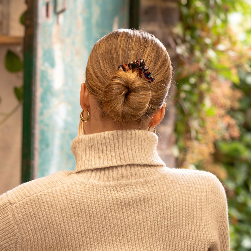 Person with a bun wearing a beige sweater in an outdoor setting